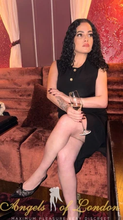 Londno escort Sharma in black dress with wine